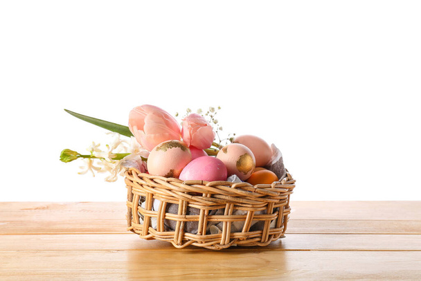 Panier cadeau avec des œufs de Pâques peints et des fleurs sur la table sur fond blanc - Photo, image