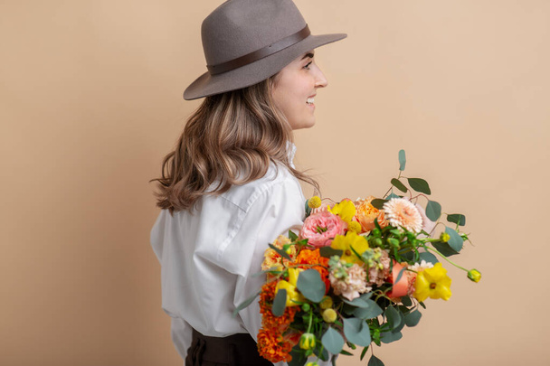 mujer feliz en fieltro sombrero sosteniendo ramo de flores - Foto, imagen