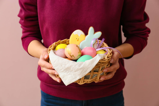 Woman holding gift basket with painted Easter eggs and cookies on pink background - Foto, imagen