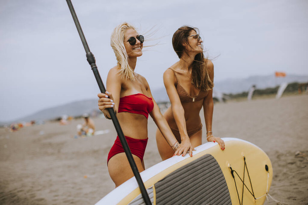 Two pretty young women with paddle board on the beach on a summer day - Foto, immagini