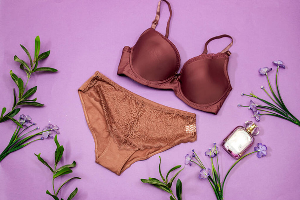 elegant woman lace bra with panties, perfume bottle and flowers on purple background. Stylish lingerie flat lay - Fotoğraf, Görsel
