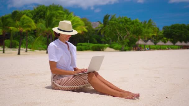 Успешная деловая женщина в жёлтой шляпе работает на ноутбуке у моря. Красивая леди печатает на компьютере в летний день на открытом воздухе. Концепция фриланса, путешествий и праздников. - Кадры, видео