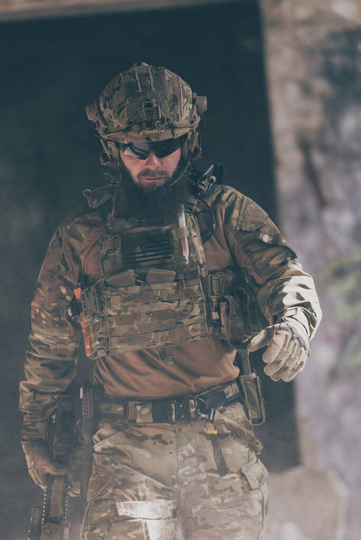 A bearded soldier in a special forces uniform walks through an abandoned building after a successful mission. Selection focus. High-quality photo - Foto, Imagen