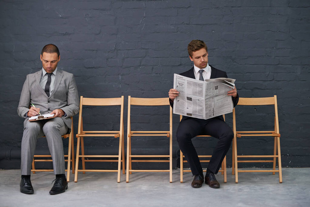 Separando la competencia. Foto de una fila de sillas con dos hombres de negocios sentados ligeramente separados. - Foto, Imagen