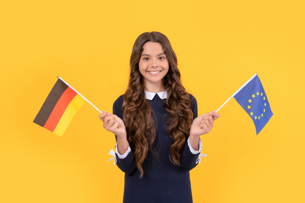 smiling child hold european union and german flag yellow background, studying abroad - Photo, Image