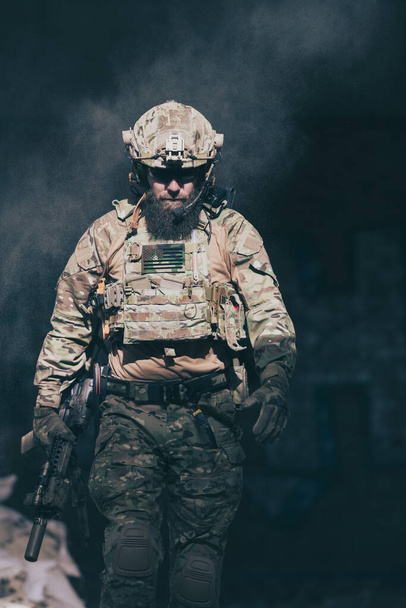 A bearded soldier in a special forces uniform walks through an abandoned building after a successful mission. Selection focus. High-quality photo - Foto, imagen