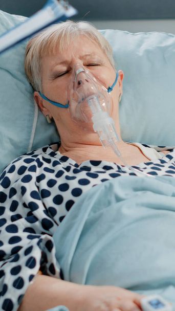 Ηλικιωμένη γυναίκα με συμπτώματα από κορωνοϊό φορώντας μάσκα οξυγόνου - Φωτογραφία, εικόνα