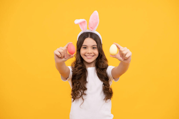 smiling kid in bunny ears hold eggs on yellow background, easter - Photo, Image