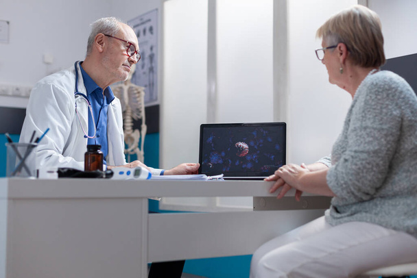 Médico mostrando ilustração de bactérias coronavírus no laptop para paciente no gabinete - Foto, Imagem
