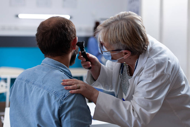 Κοντινό πλάνο του γιατρού που χρησιμοποιεί ωτοσκόπιο για να κάνει ακρόαση με τον ασθενή - Φωτογραφία, εικόνα