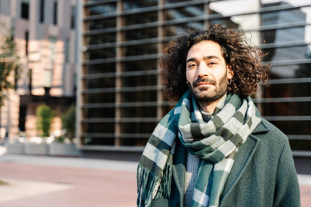 Young stylish professional man with long curly hair wearing a green scarf in the city in winter - Foto, imagen