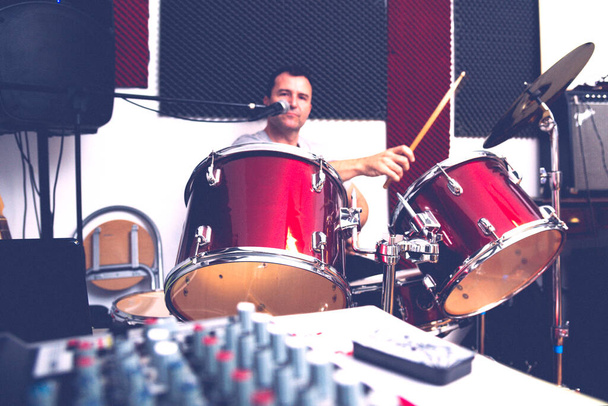 DRUMMER REHEARSING ALONE IN FRONT OF HIS RED DRUM KIT WITH THE MIXING CONSOLE - Photo, Image