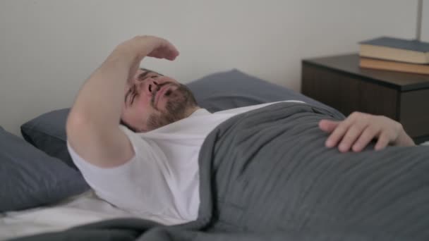 Młody człowiek odczuwa ból głowy podczas snu w łóżku - Materiał filmowy, wideo
