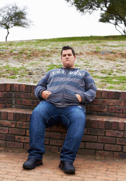 Ein fettleibiger Mann sitzt an einem Wintertag draußen, die Hände in den Taschen.. - Foto, Bild