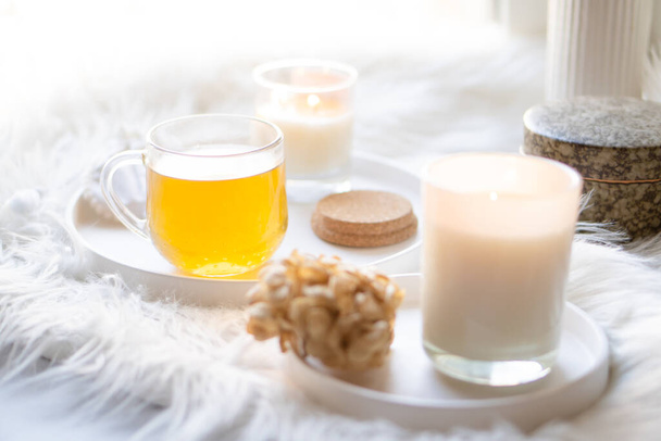 Šálek bylinkového čaje a hořící svíčky na kulatém bílém ozdobném podnosu - Fotografie, Obrázek