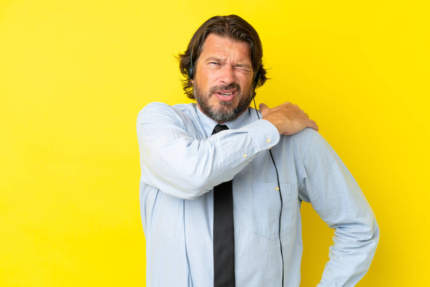 Hombre holandés de telemarketer que trabaja con un auricular aislado en el fondo amarillo que sufre de dolor en el hombro por haber hecho un esfuerzo - Foto, imagen