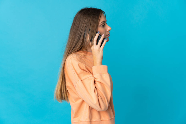 Nuori liettualainen nainen sinisellä taustalla keskustelee matkapuhelimen kanssa jonkun kanssa - Valokuva, kuva