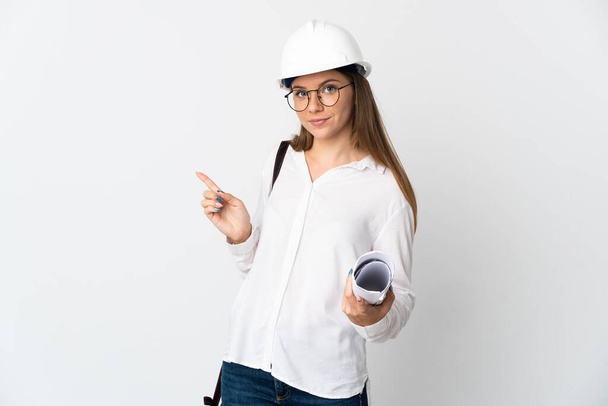 Young Lithuanian architect woman with helmet and holding blueprints isolated on white background pointing finger to the side - Photo, Image