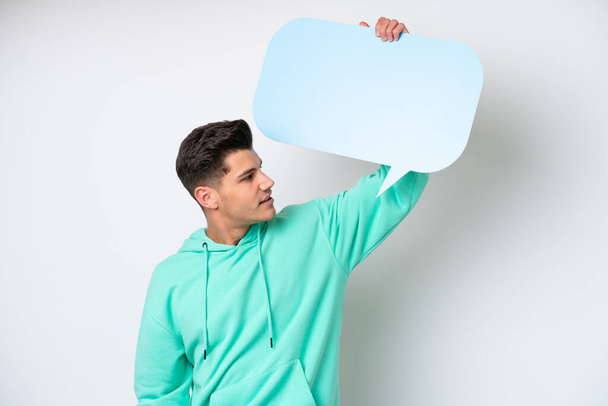Young handsome caucasian man isolated on white bakcground holding an empty speech bubble - Zdjęcie, obraz