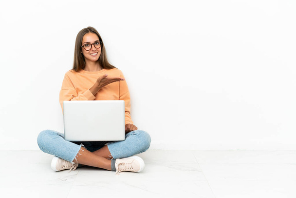 Dizüstü bilgisayarı olan genç bir kadın yere oturmuş gülümserken bir fikir sunuyor. - Fotoğraf, Görsel