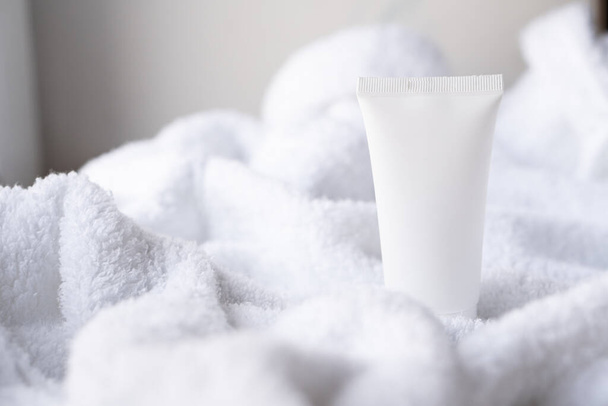 Clean white cosmetic cream tube on fluffy white cotton towel background, mock-up and design ready - 写真・画像