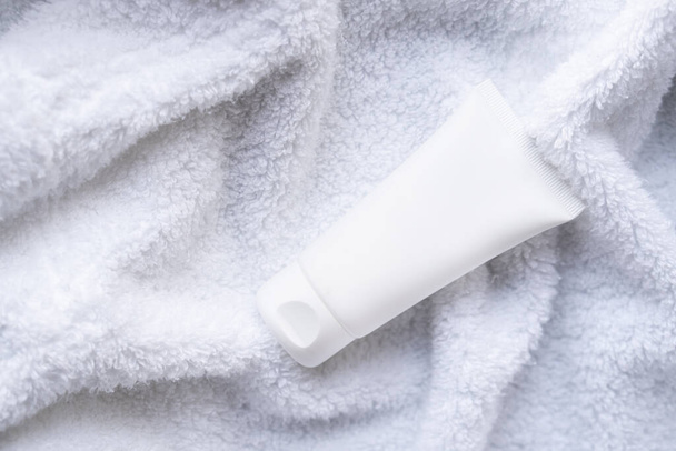 Tubo de crema cosmética blanca limpia sobre fondo de toalla de algodón blanco esponjoso, maqueta y diseño listo - Foto, imagen