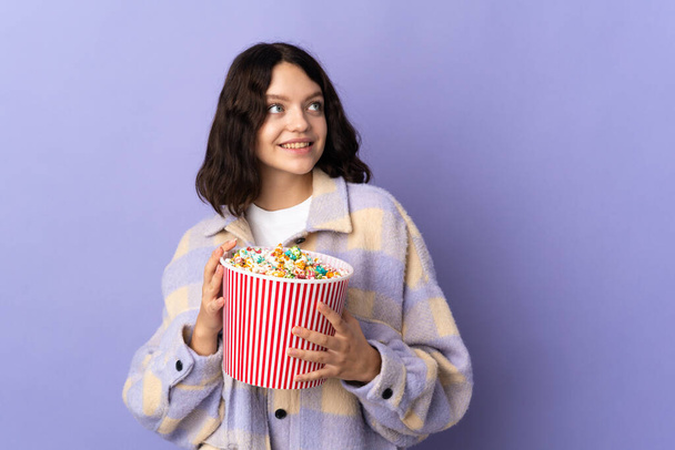 tiener Oekraïense meisje geïsoleerd op paarse achtergrond met een grote emmer popcorn - Foto, afbeelding