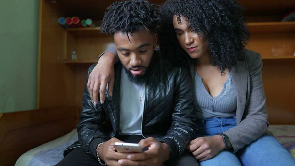 1人の黒人夫婦が寝室で一緒に携帯電話を見て - 写真・画像