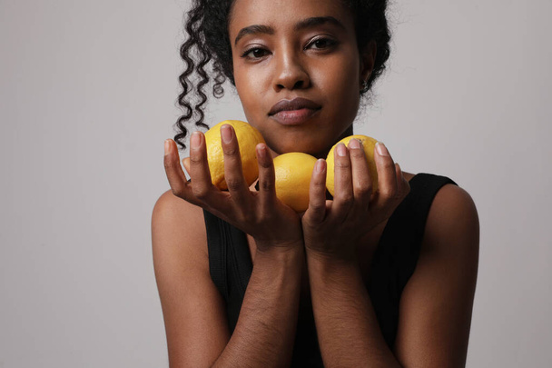 Oříznutá fotografie mladé ženy pózující se třemi částmi citronu na bílé stěně. - Fotografie, Obrázek