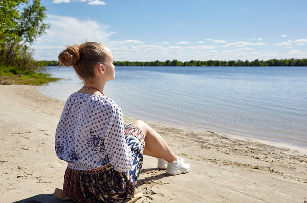 Girl sitting on the coast and looking into the distance. Young woman resting at water. Enjoy life, having fun, leisure, relaxation, lifestyle concept - Foto, immagini