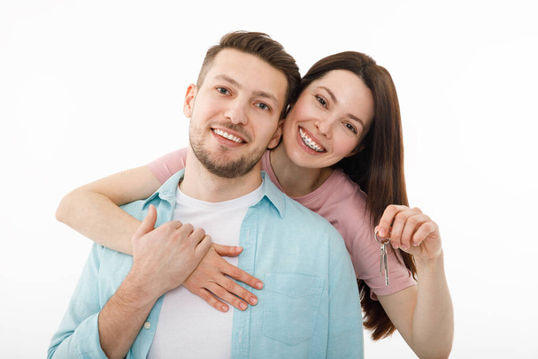 Um jovem casal alegre está abraçando na cozinha, segurando as chaves de uma nova casa em suas mãos. Os recém-casados felizes mudaram-se para um novo apartamento, fizeram uma hipoteca, mudaram-se.. - Foto, Imagem