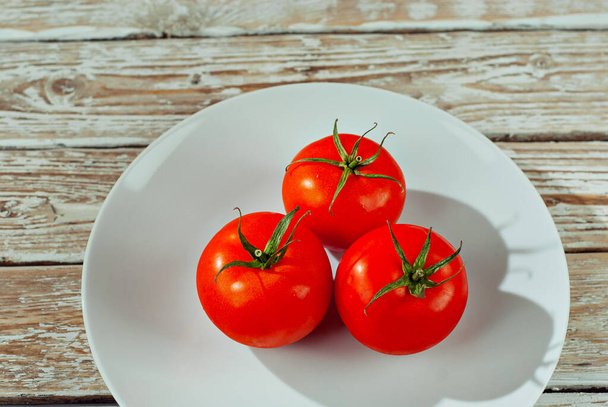 Tomatoes in a white plate. Vegetables on a white wooden table. Tomatoes on an old shabby board.  - 写真・画像
