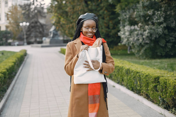 Young black woman in a coat standing outside holding a bag with a bread - Photo, Image