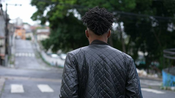 A pensive young black man walking outside in urban street a thoughtful African person - 写真・画像