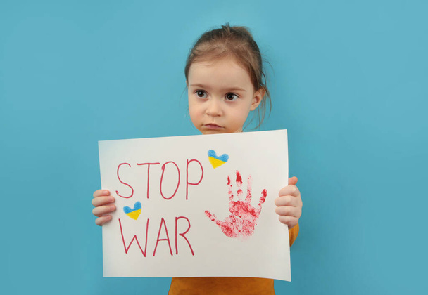 Portrait little girl calls to Stop war in Ukraine, raises banner with inscription stop the war in Ukraine standing on blue background. No war, stop war, russian aggression. Ukrainian patriot. Top view - Fotó, kép