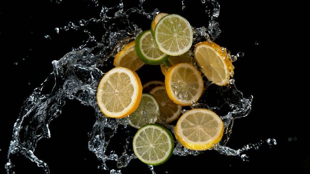 Заморожувати рух нарізаних лімітів та лимонів у бризках води. Ізольовані на чорному тлі
. - Фото, зображення