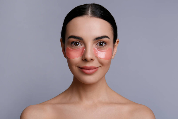 Beautiful young woman with under eye patches on grey background - Φωτογραφία, εικόνα