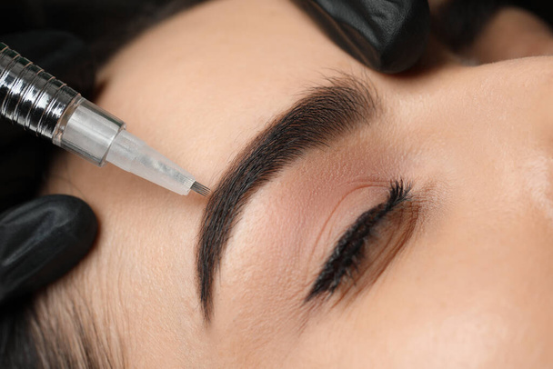 Young woman undergoing procedure of permanent eyebrow makeup in salon, closeup - Foto, imagen
