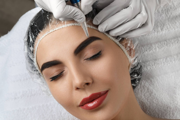 Young woman undergoing procedure of permanent eyebrow makeup in salon, closeup - Photo, image