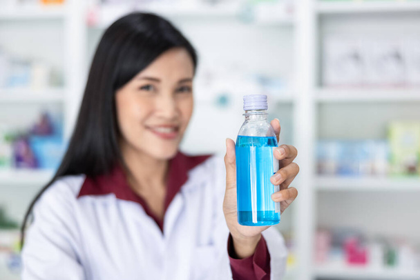 azjatycki aptekarka pokazać butelki żel do rąk w aptece Tajlandia zbliżenie i selektywne ostrość niebieski żel na strony farmaceuta  - Zdjęcie, obraz