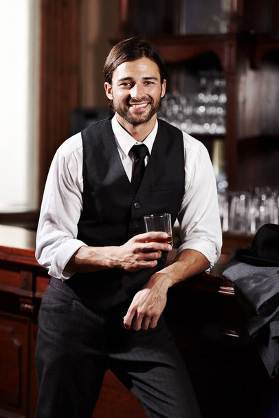 Ontspannen tijdens het drinken. Portret van een goed geklede jongeman die met een drankje in een bar staat. - Foto, afbeelding