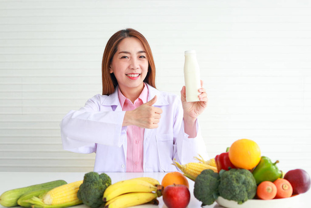美しいアジアの栄養士が彼女の机に座って果物や野菜と栄養ボトルを保持しています。栄養価の高い食事の準備やアドバイスをしました。ヘルスケアの概念 - 写真・画像
