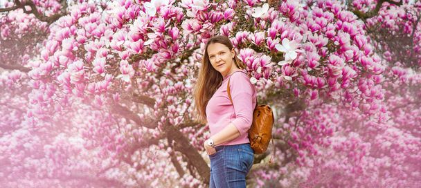  Portret van mooie jonge vrouw in de buurt van bloeiende magnolia boom buitenshuis  - Foto, afbeelding