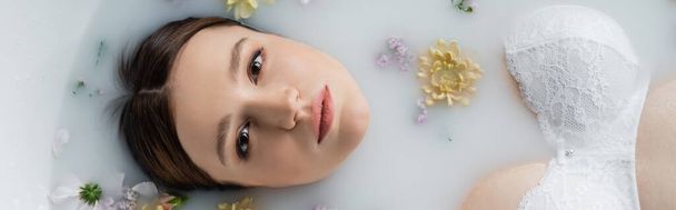 Top view of young woman in bra looking at camera in milk bath with flowers, banner  - Foto, Imagem