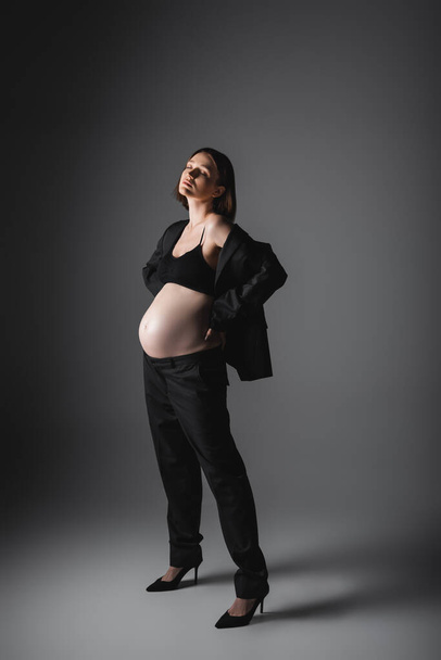 Mulher grávida elegante em saltos altos e terno em pé sobre fundo cinza - Foto, Imagem
