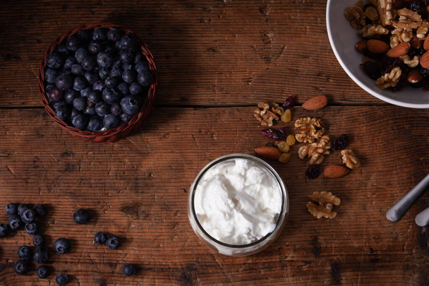 cup of greek yogurt with blueberries and mixed nuts on wooden table - Foto, afbeelding