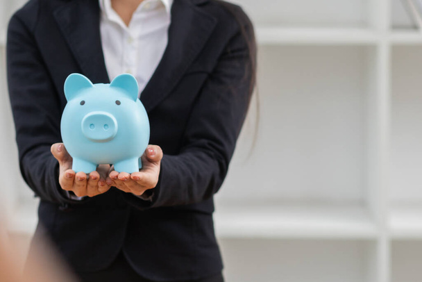 Een jonge zakenman of investeerder houdt een blauwe spaarpot in haar hand. De spaarpot is een idee voor het sparen of accumuleren van activa voor beleggingen of voor pensionering. - Foto, afbeelding