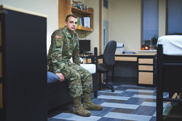 Jotkut kutsuvat sitä asuntolaksi, minä kodiksi. Nuori sotilas istuu sängyllään sotilasakatemian asuntolassa.. - Valokuva, kuva