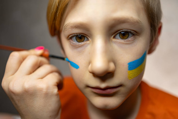 uma criança contra a guerra, um menino com uma bandeira pintada da Ucrânia em suas bochechas - Foto, Imagem
