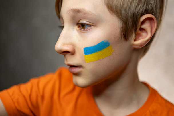 překvapené dítě proti válce, s namalovanou vlajkou Ukrajiny na tvářích - Fotografie, Obrázek
